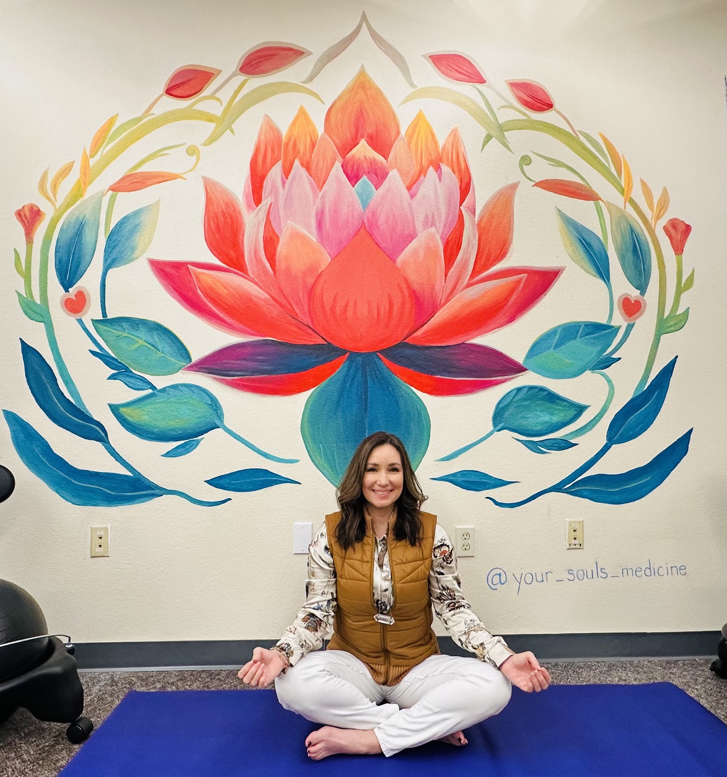 Nicole Alexander seated on the grass with shamanic drum, smiling warmly in golden light